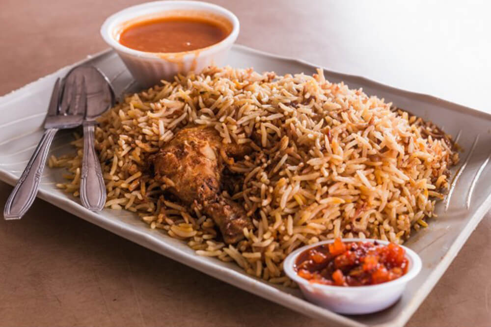 A plate of Nasi Briyani with chicken and chilli sauce on a table
